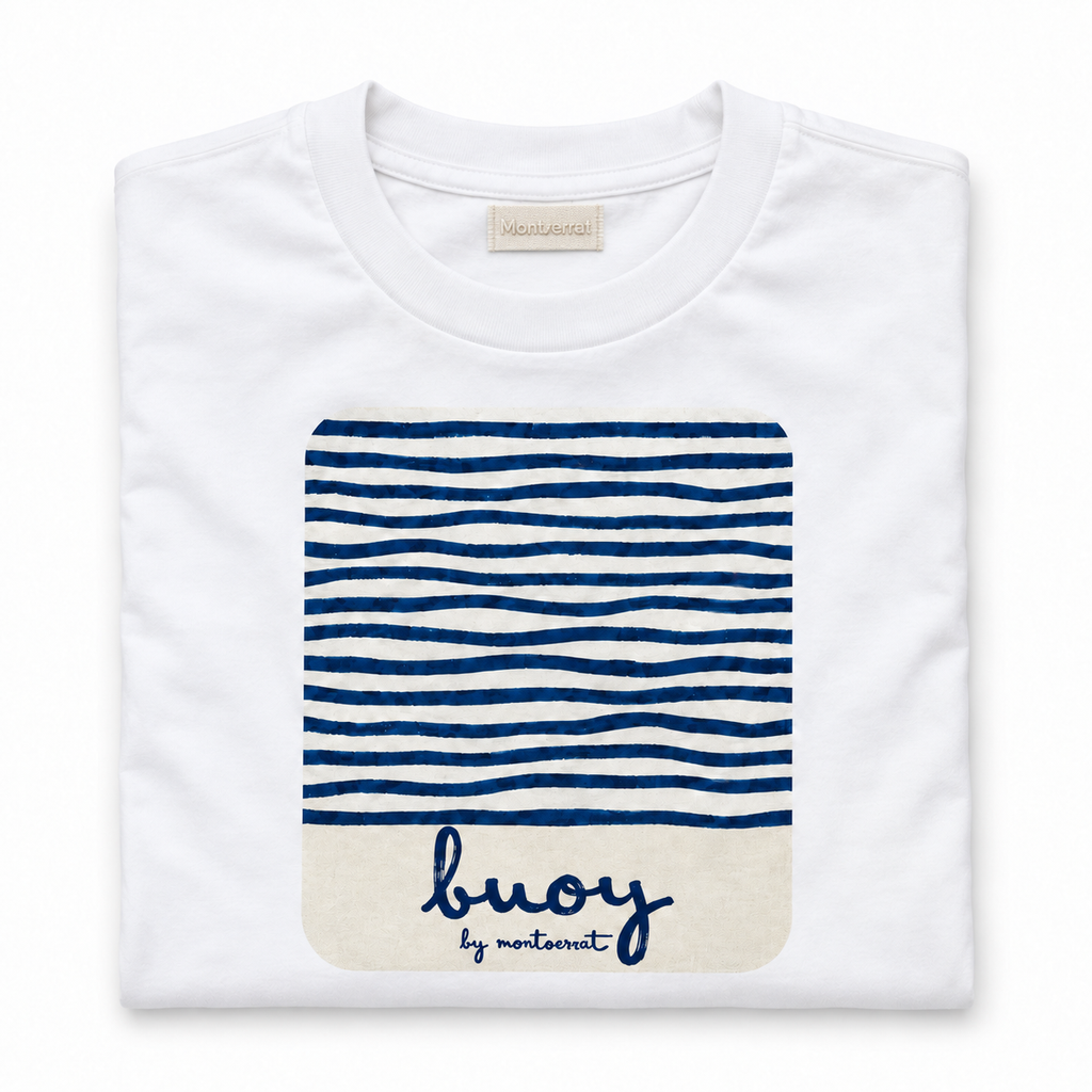 A folded white crewneck t-shirt by Montserrat, featuring a navy blue and white striped graphic on the front with a cream-coloured bottom section containing the brand name 'buoy by Montserrat' in navy script.