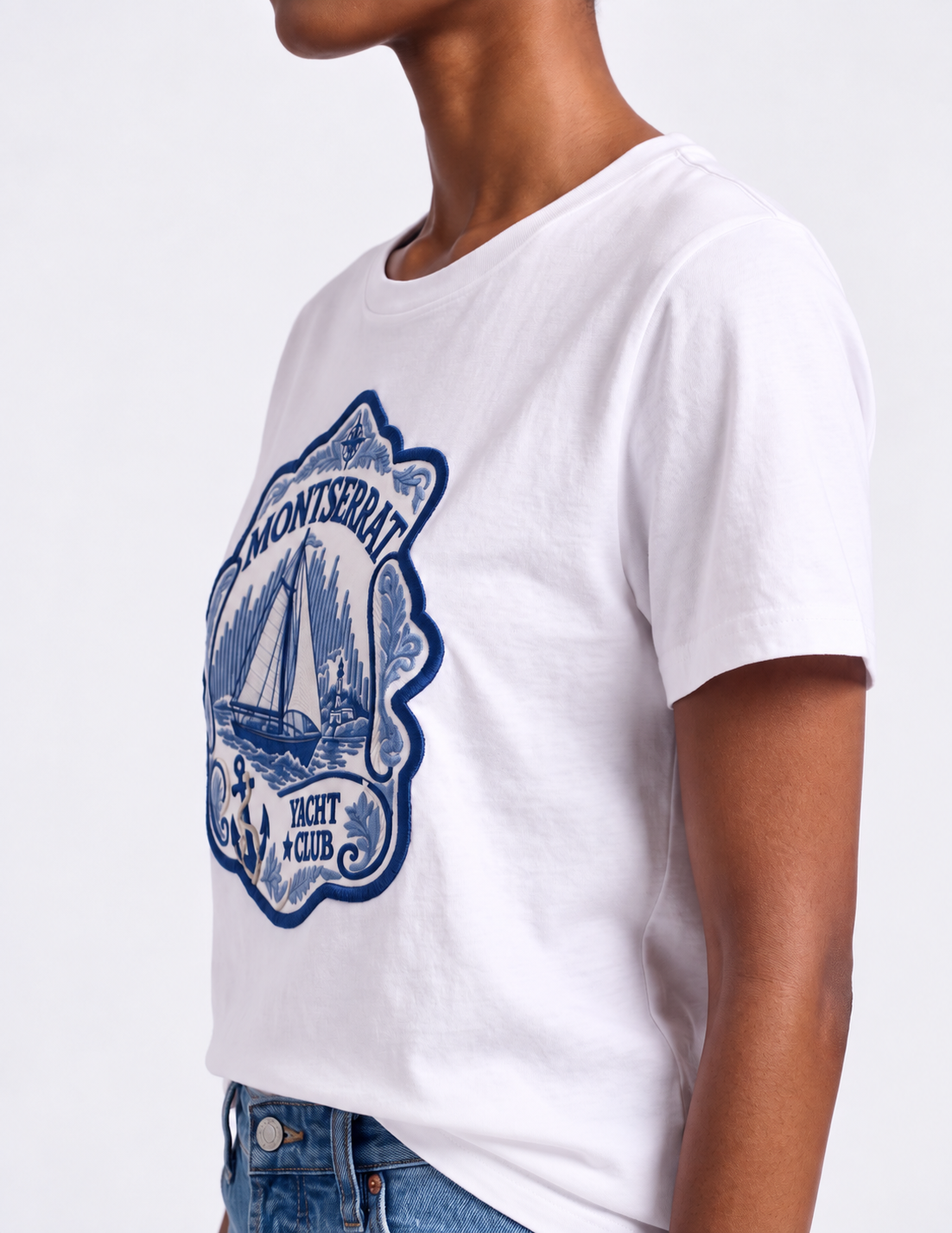 Back view of a model wearing a white Montserrat T-shirt with a small dark logo and light blue jeans in a studio.